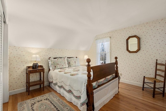 bedroom featuring vaulted ceiling, baseboards, wood finished floors, and wallpapered walls