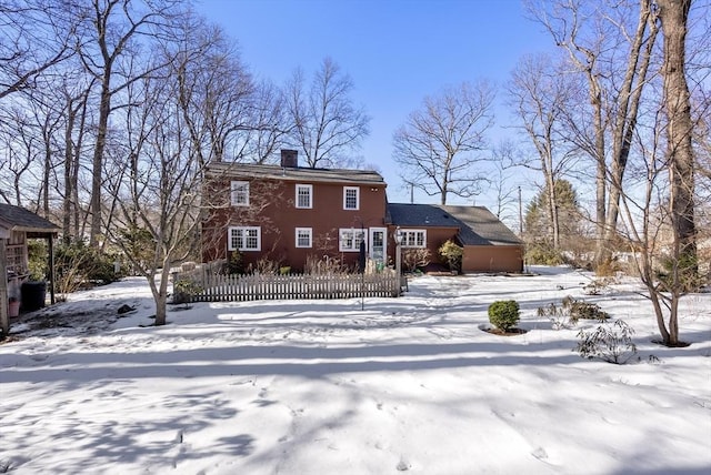 snow covered house featuring a chimney and fence