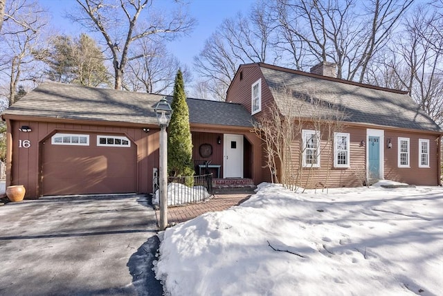 colonial inspired home with a garage, a shingled roof, a gambrel roof, driveway, and a chimney