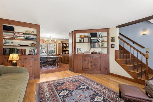 living area with light wood-style flooring, stairway, baseboards, and an inviting chandelier