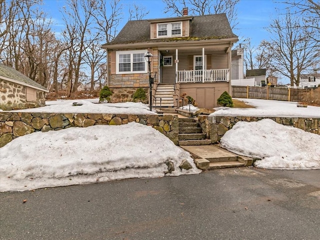 bungalow-style home with covered porch, fence, stone siding, stairway, and a chimney