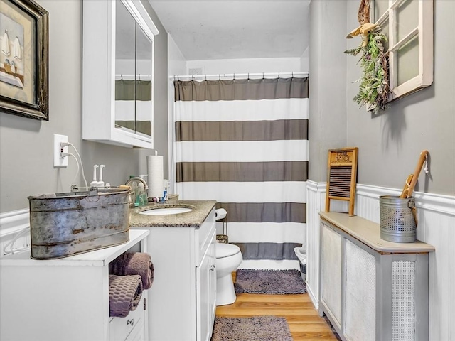 full bath with toilet, a wainscoted wall, wood finished floors, vanity, and a shower with curtain