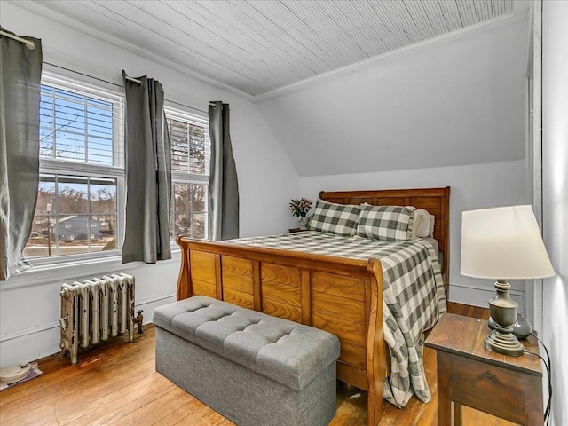 bedroom with radiator heating unit, vaulted ceiling, and hardwood / wood-style floors