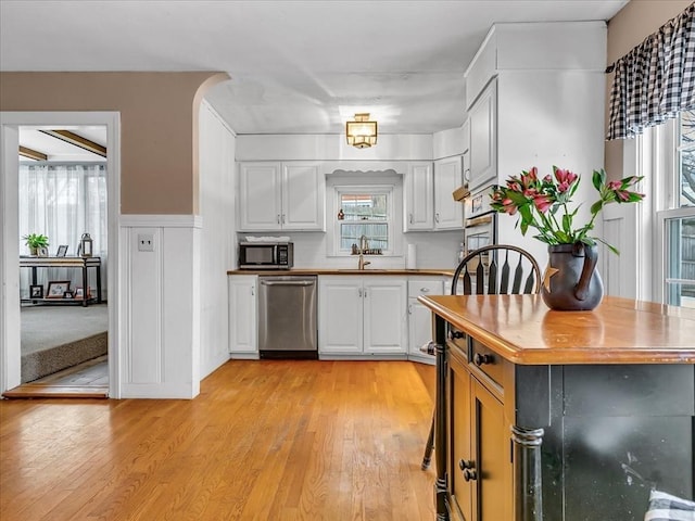 kitchen featuring white cabinets, dishwasher, a wainscoted wall, light wood-type flooring, and a sink