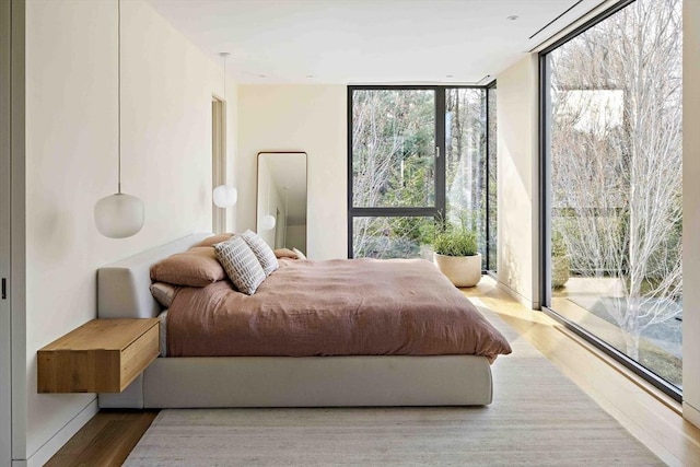 bedroom with expansive windows, wood finished floors, and access to exterior
