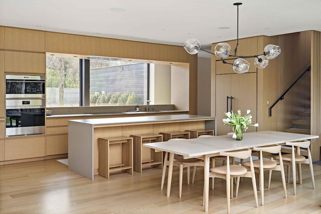 kitchen with double oven, a chandelier, light wood-style floors, a sink, and light brown cabinets
