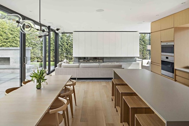 kitchen featuring a wall of windows, light brown cabinetry, stainless steel double oven, modern cabinets, and light wood finished floors