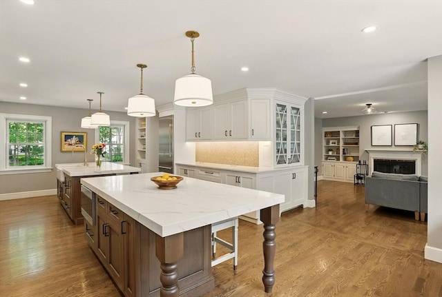 171 Brentwood Cir, North Andover, MA 01845 - kitchen with a kitchen island with sink, baseboards, a glass covered fireplace, white cabinetry, and glass insert cabinets