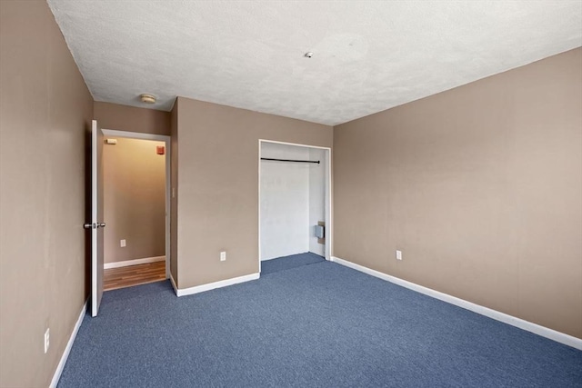 unfurnished bedroom featuring a textured ceiling, dark carpet, and a closet