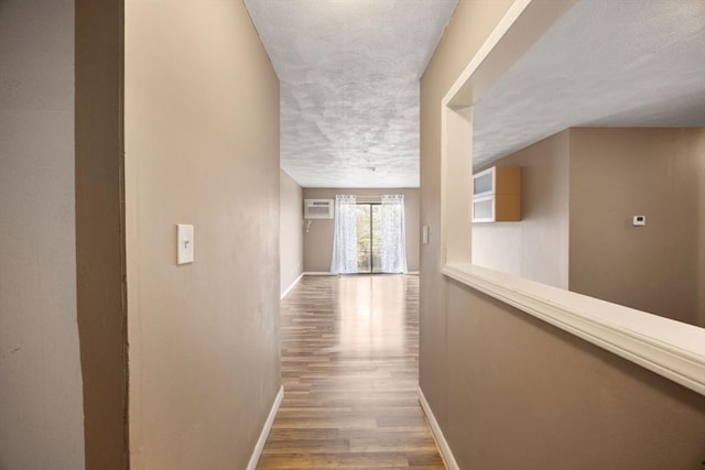 hall featuring hardwood / wood-style flooring, a textured ceiling, and a wall unit AC