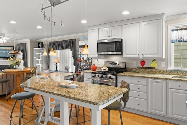 16 Ocean St Unit A, Salisbury, MA 01952 - kitchen featuring appliances with stainless steel finishes, ornamental molding, a breakfast bar area, light wood finished floors, and white cabinets
