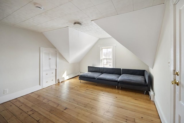 interior space with a baseboard radiator, vaulted ceiling, and light wood-type flooring