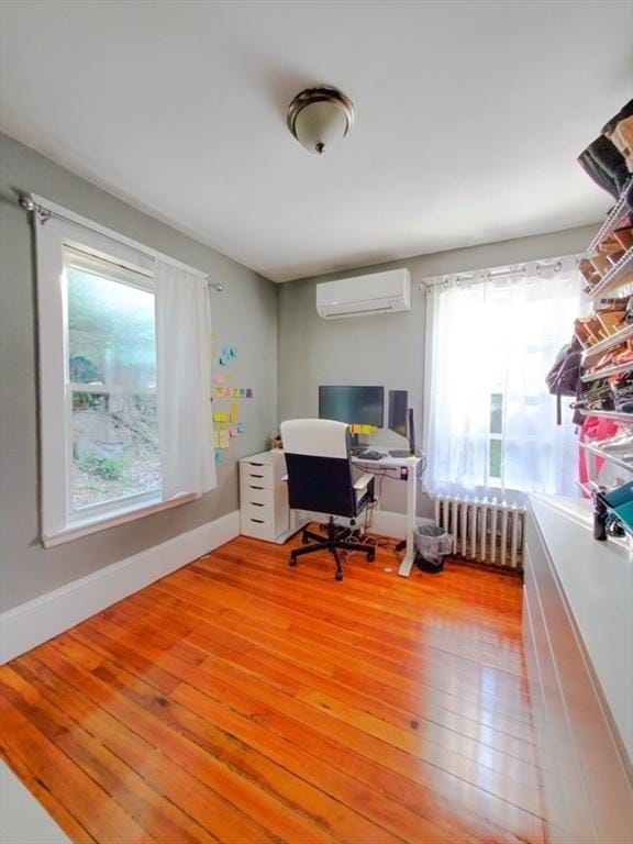 office space featuring light hardwood / wood-style floors, an AC wall unit, a healthy amount of sunlight, and radiator