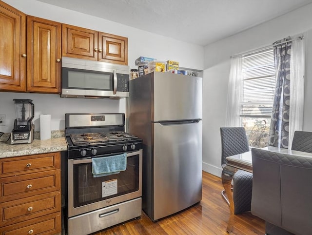 kitchen with light hardwood / wood-style floors, light stone counters, and stainless steel appliances