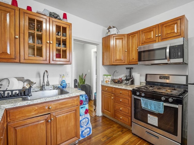 kitchen with light stone counters, sink, stainless steel appliances, and wood-type flooring