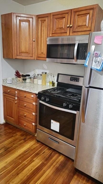 kitchen featuring light stone counters, stainless steel appliances, and dark wood-type flooring