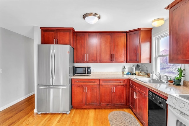 kitchen with light wood-type flooring, stainless steel appliances, light stone counters, and sink