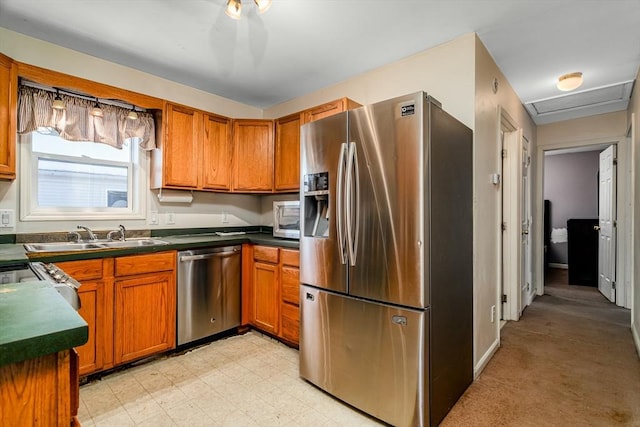 kitchen with brown cabinetry, dark countertops, stainless steel appliances, light floors, and a sink