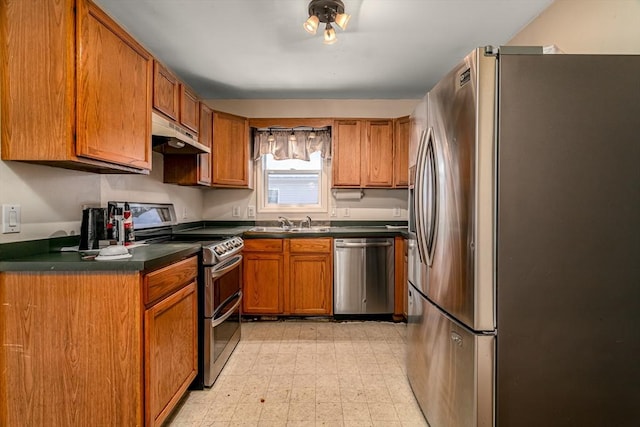 kitchen with appliances with stainless steel finishes, dark countertops, brown cabinets, and under cabinet range hood