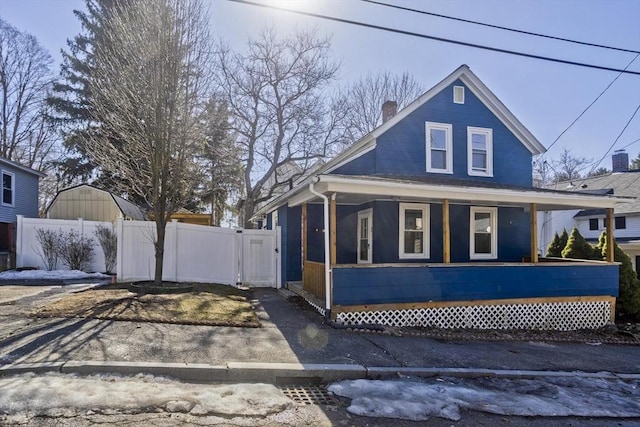 bungalow-style house with a gate, covered porch, a chimney, and fence