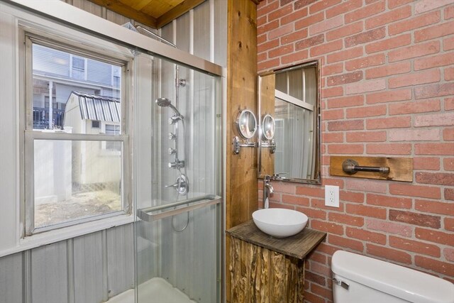 full bathroom with a shower stall, a healthy amount of sunlight, and brick wall