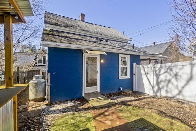 exterior space featuring roof with shingles, a chimney, and fence