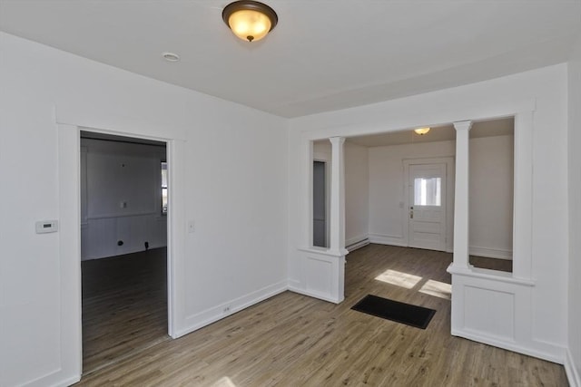 unfurnished room featuring decorative columns, baseboards, and wood finished floors