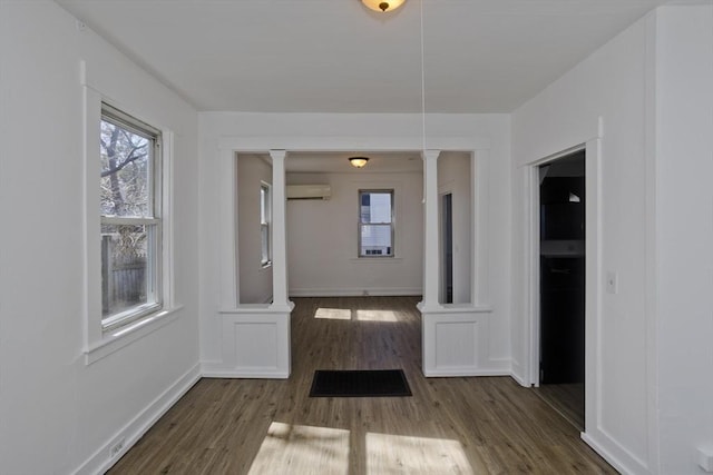 interior space with ornate columns, baseboards, wood finished floors, and a wall unit AC