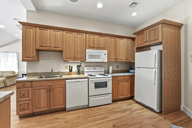 kitchen with white appliances, light wood finished floors, visible vents, brown cabinets, and a sink