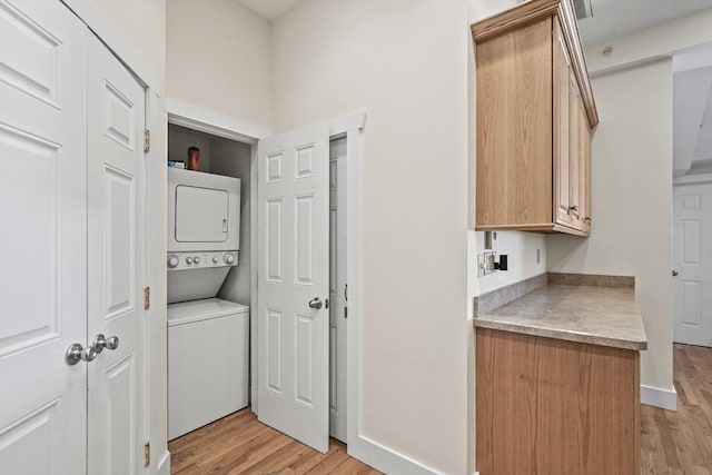 washroom featuring baseboards, laundry area, light wood-type flooring, and stacked washer / drying machine