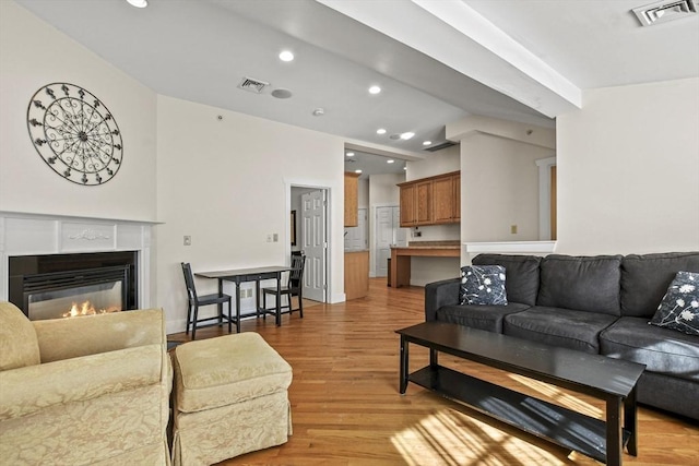 living area with light wood-style floors, visible vents, vaulted ceiling, and a glass covered fireplace