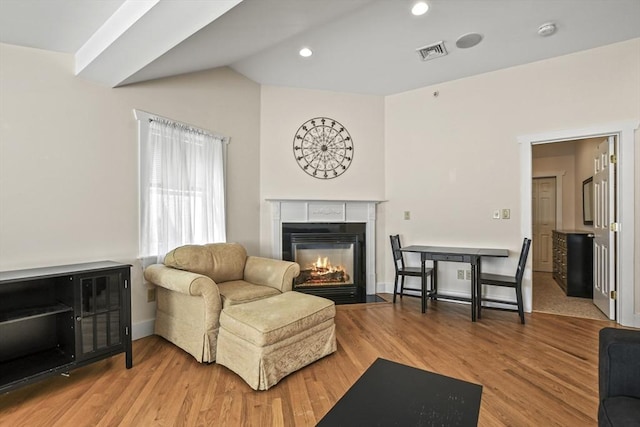 living room featuring lofted ceiling, wood finished floors, a fireplace with flush hearth, visible vents, and baseboards