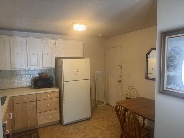 kitchen with light countertops, white cabinets, freestanding refrigerator, and backsplash