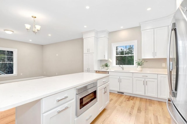 kitchen featuring built in microwave, sink, pendant lighting, white cabinets, and stainless steel refrigerator