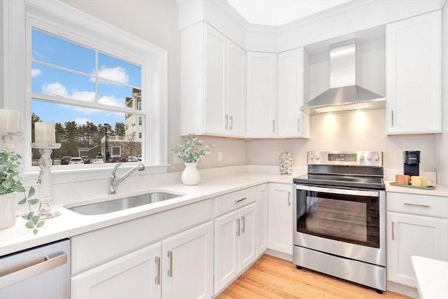 kitchen with appliances with stainless steel finishes, sink, wall chimney range hood, white cabinets, and light hardwood / wood-style floors