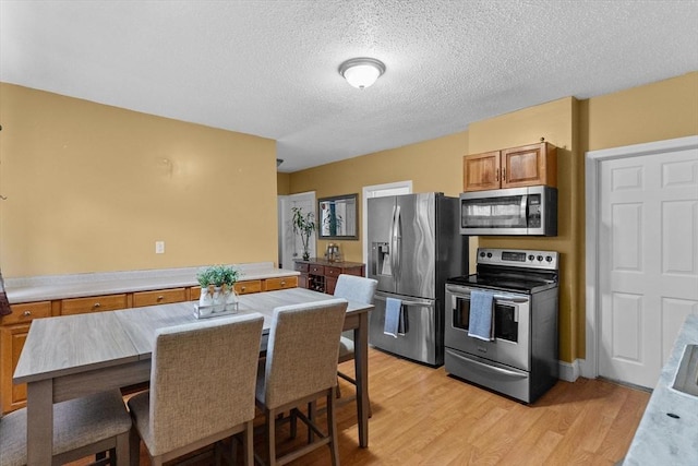 kitchen with stainless steel appliances, light wood-style floors, brown cabinets, a textured ceiling, and light countertops