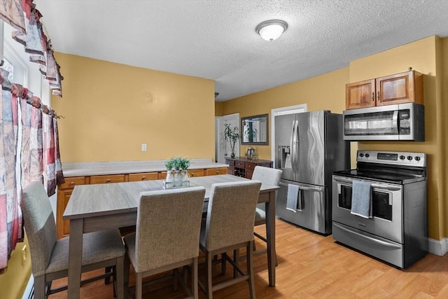 kitchen with stainless steel appliances, brown cabinetry, light wood-style flooring, a textured ceiling, and light countertops