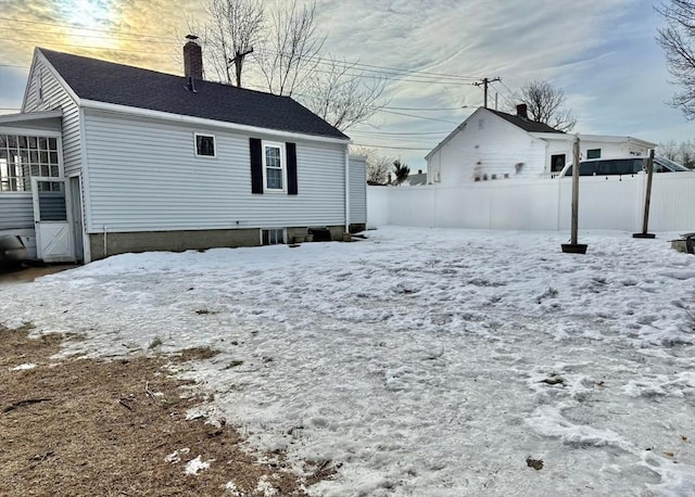 snow covered back of property with a sunroom, a chimney, fence, and roof with shingles