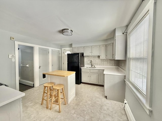 kitchen featuring tasteful backsplash, a kitchen breakfast bar, freestanding refrigerator, wooden counters, and a sink