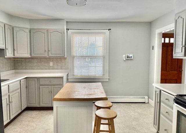 kitchen with a baseboard heating unit, light countertops, a kitchen bar, and gray cabinets