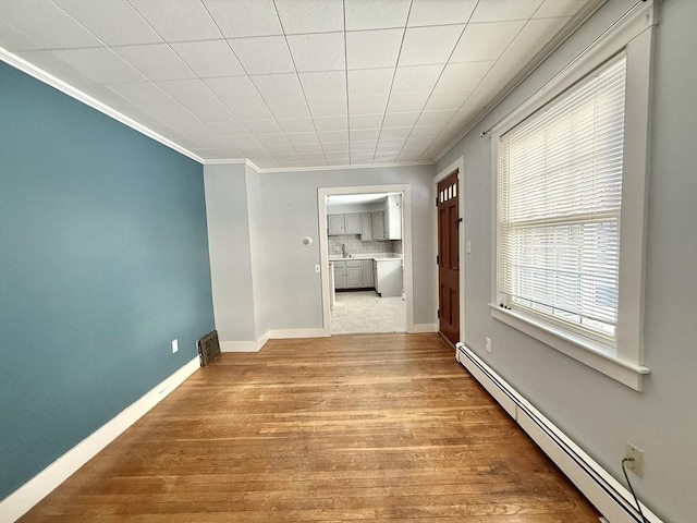 empty room featuring baseboards, baseboard heating, wood finished floors, and crown molding