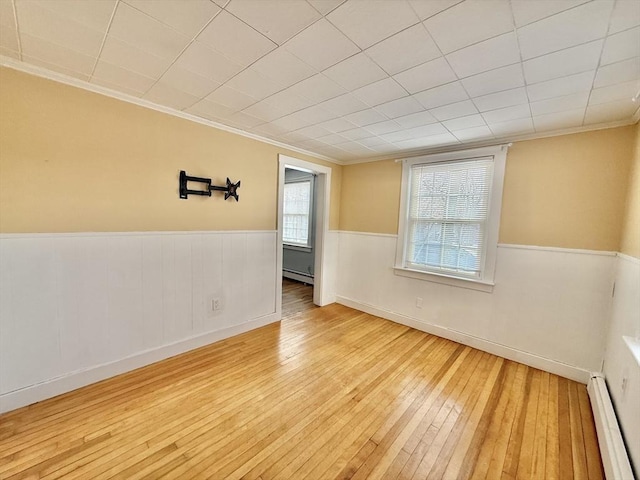 spare room featuring ornamental molding, a baseboard radiator, wood-type flooring, and wainscoting