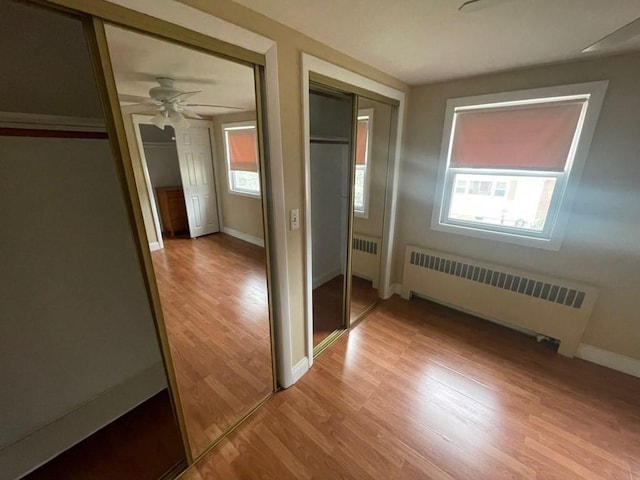 unfurnished bedroom featuring radiator, multiple windows, and light wood-type flooring