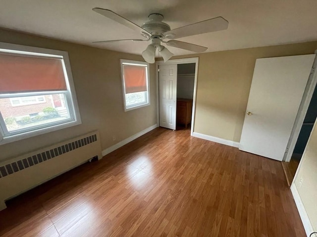 unfurnished bedroom featuring hardwood / wood-style floors, a closet, radiator, and ceiling fan