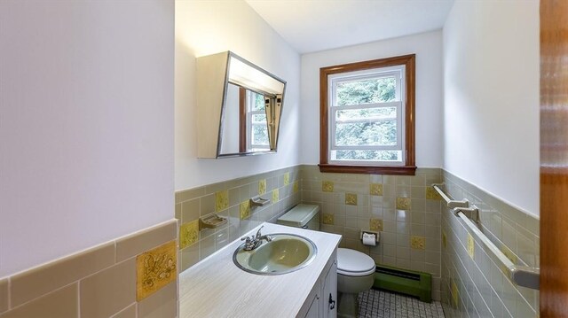 bathroom featuring baseboard heating, vanity, toilet, and tile walls