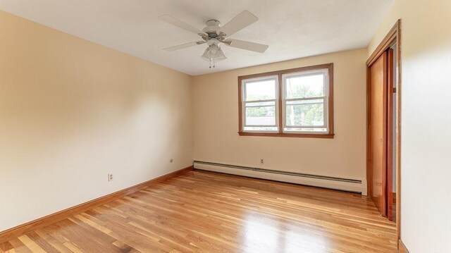 empty room featuring a baseboard heating unit, ceiling fan, and light wood-type flooring