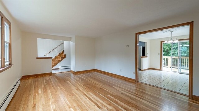 unfurnished living room featuring baseboard heating, a chandelier, and light wood-type flooring