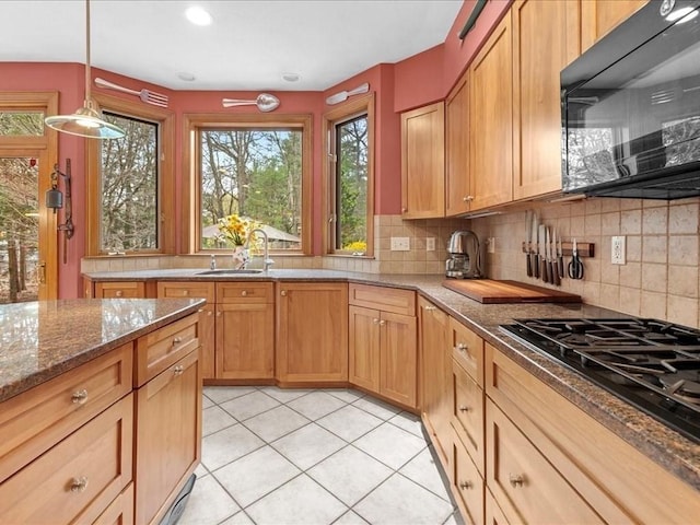 kitchen with gas cooktop, black microwave, a sink, dark stone counters, and tasteful backsplash