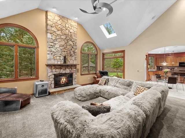living area featuring carpet floors, a fireplace, ceiling fan, high vaulted ceiling, and a skylight