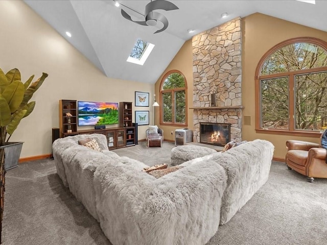 carpeted living area with a fireplace, high vaulted ceiling, a ceiling fan, baseboards, and a skylight